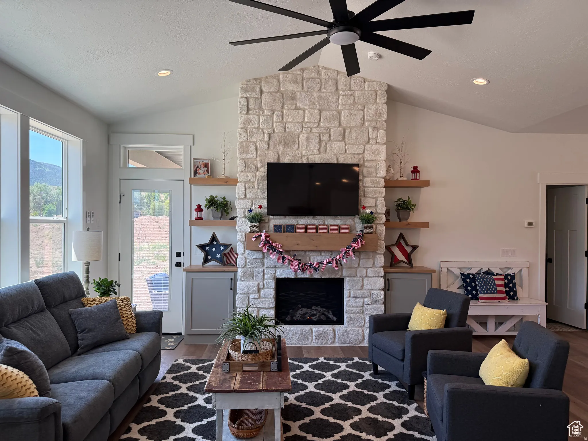 Living room with wood finished floors, a ceiling fan, a stone fireplace, and recessed lighting