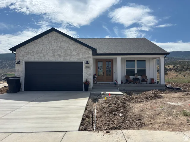 View of front of property with an attached garage, covered porch, concrete driveway, and stone siding