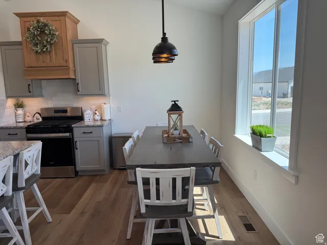 Kitchen with gray cabinets, gas stove, dark wood-type flooring, light stone countertops, and pendant lighting