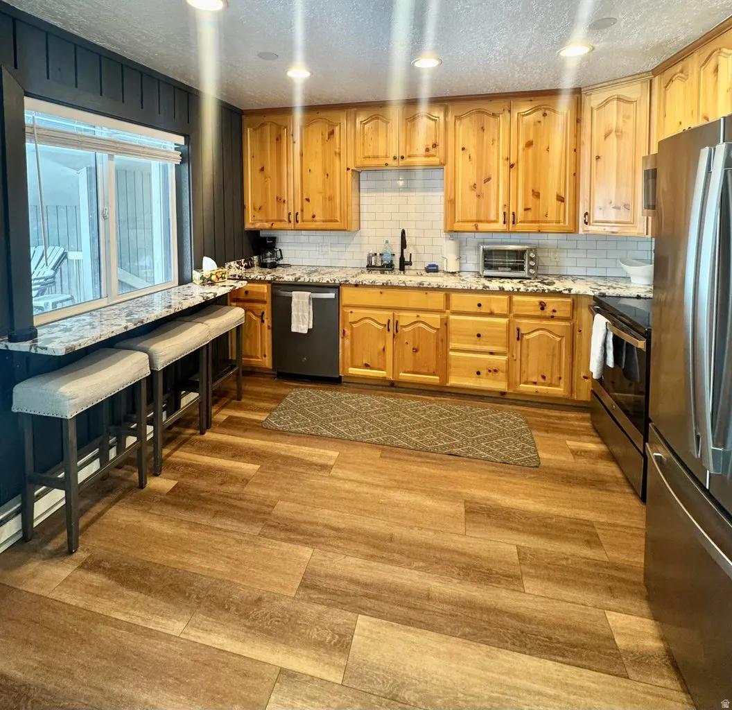 Kitchen featuring a textured ceiling, light stone countertops, stainless steel appliances, light wood finished floors, and recessed lighting