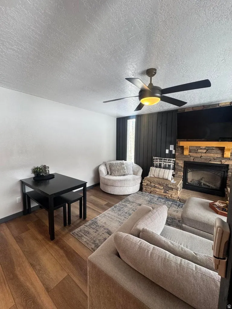 Living room with dark wood-style flooring, a fireplace, ceiling fan, and a textured ceiling