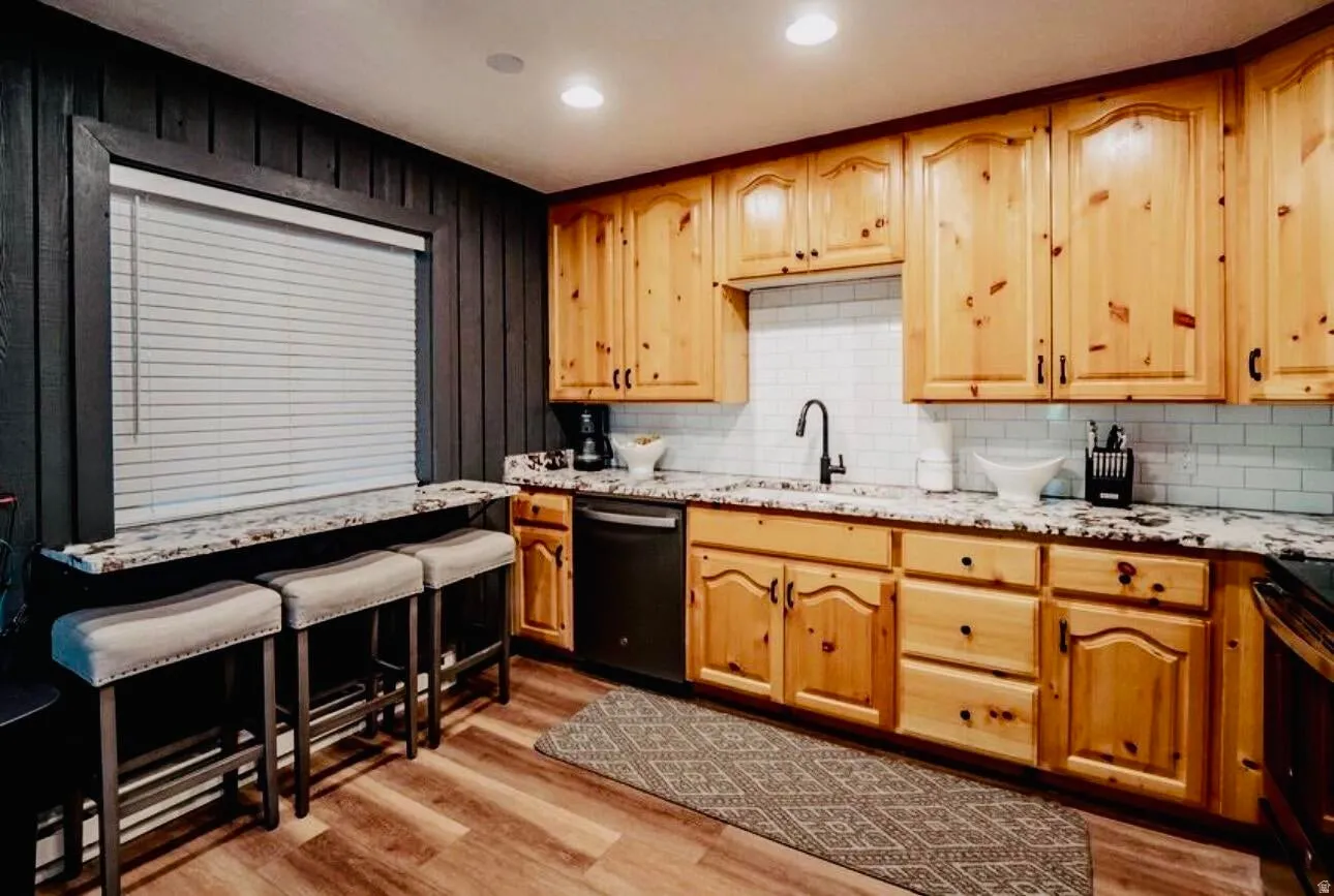 Kitchen featuring light stone counters, stainless steel stove, light wood-style floors, dishwasher, and backsplash