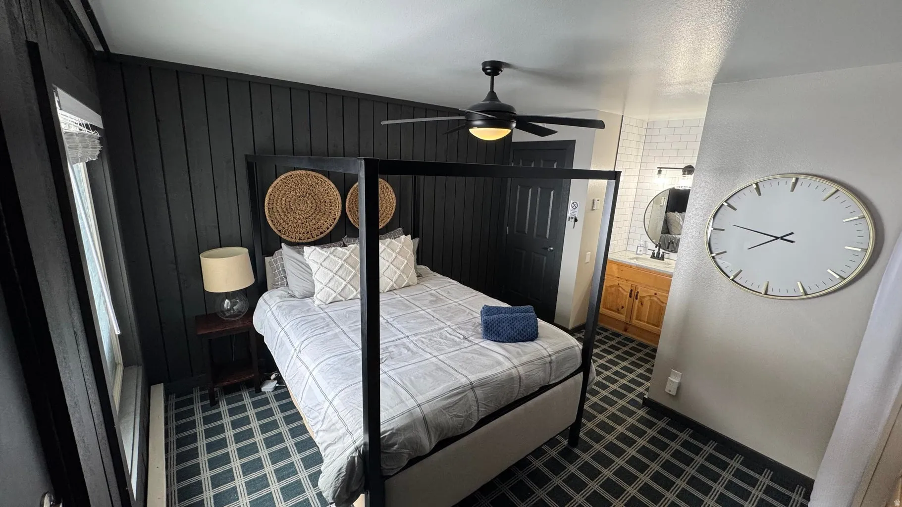 Bedroom featuring ensuite bathroom, dark colored carpet, ceiling fan, and wood walls