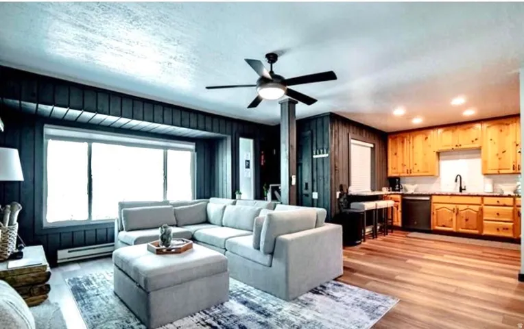 Living room with ceiling fan, light wood finished floors, baseboard heating, and wooden walls