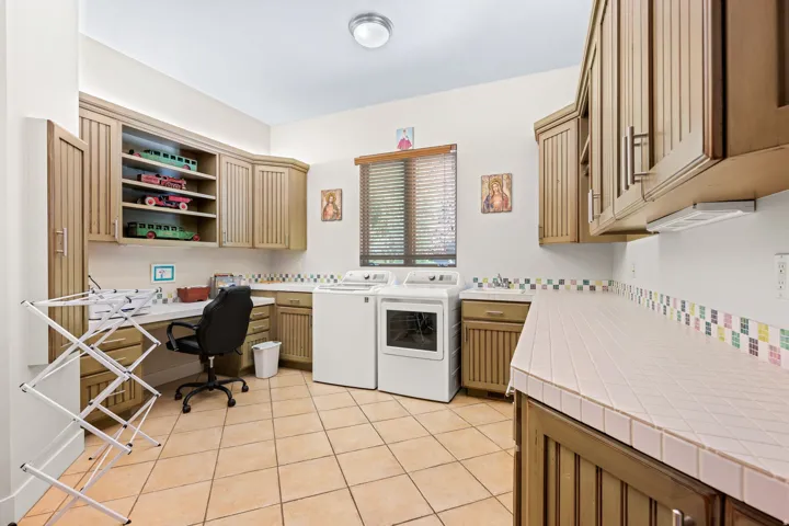 Laundry area with an office area, washing machine and dryer, light tile patterned floors, and cabinet space