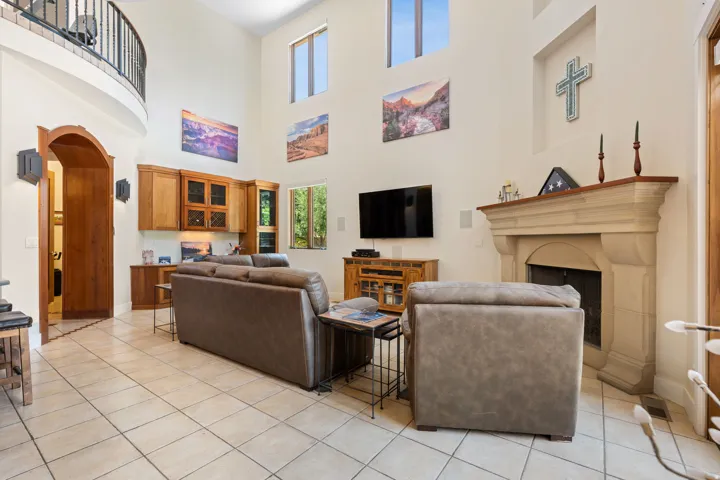 Living area featuring arched walkways, a fireplace with raised hearth, light tile patterned flooring, and a high ceiling