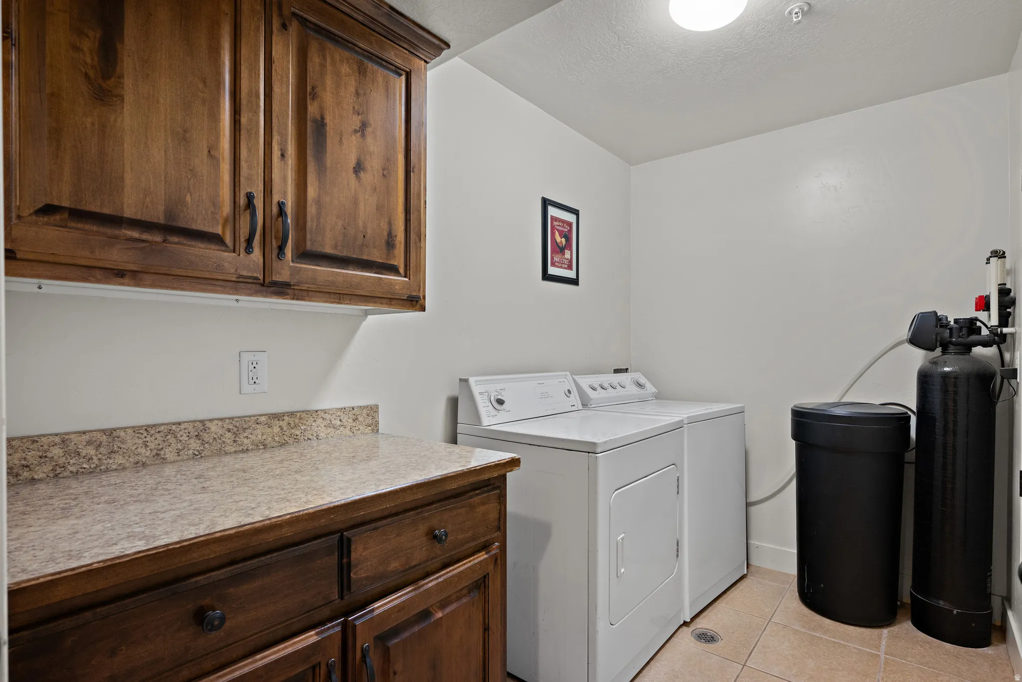 Laundry room with light tile patterned flooring, washing machine and dryer, cabinet space, and a textured ceiling