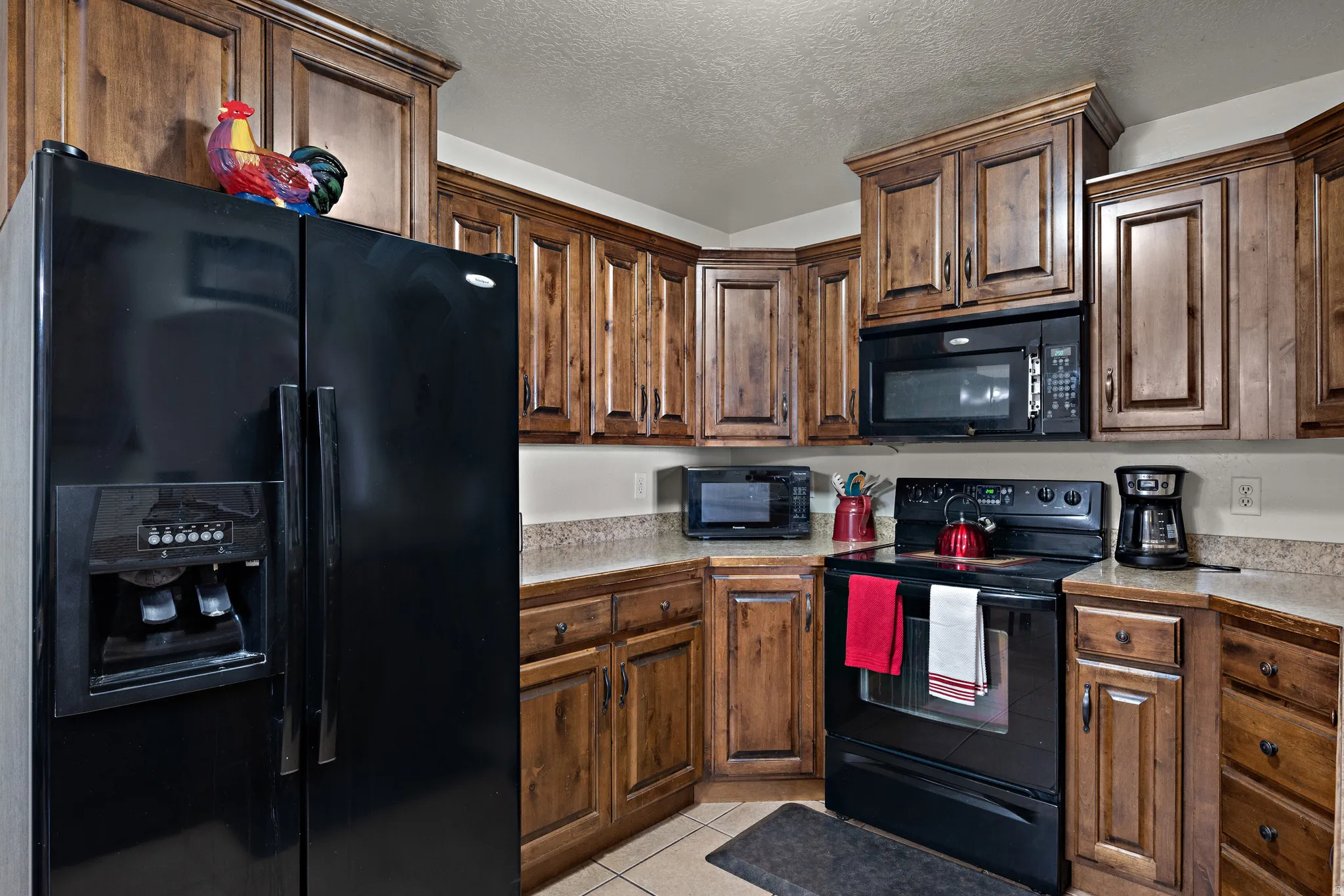 Kitchen featuring black appliances, light countertops, a textured ceiling, light tile patterned floors, and dark wood finish cabinetry