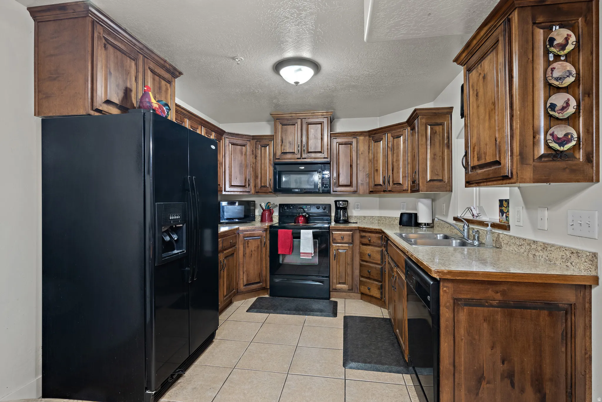 Kitchen featuring black appliances, light countertops, light tile patterned floors, a textured ceiling, and wood finish cabinetry
