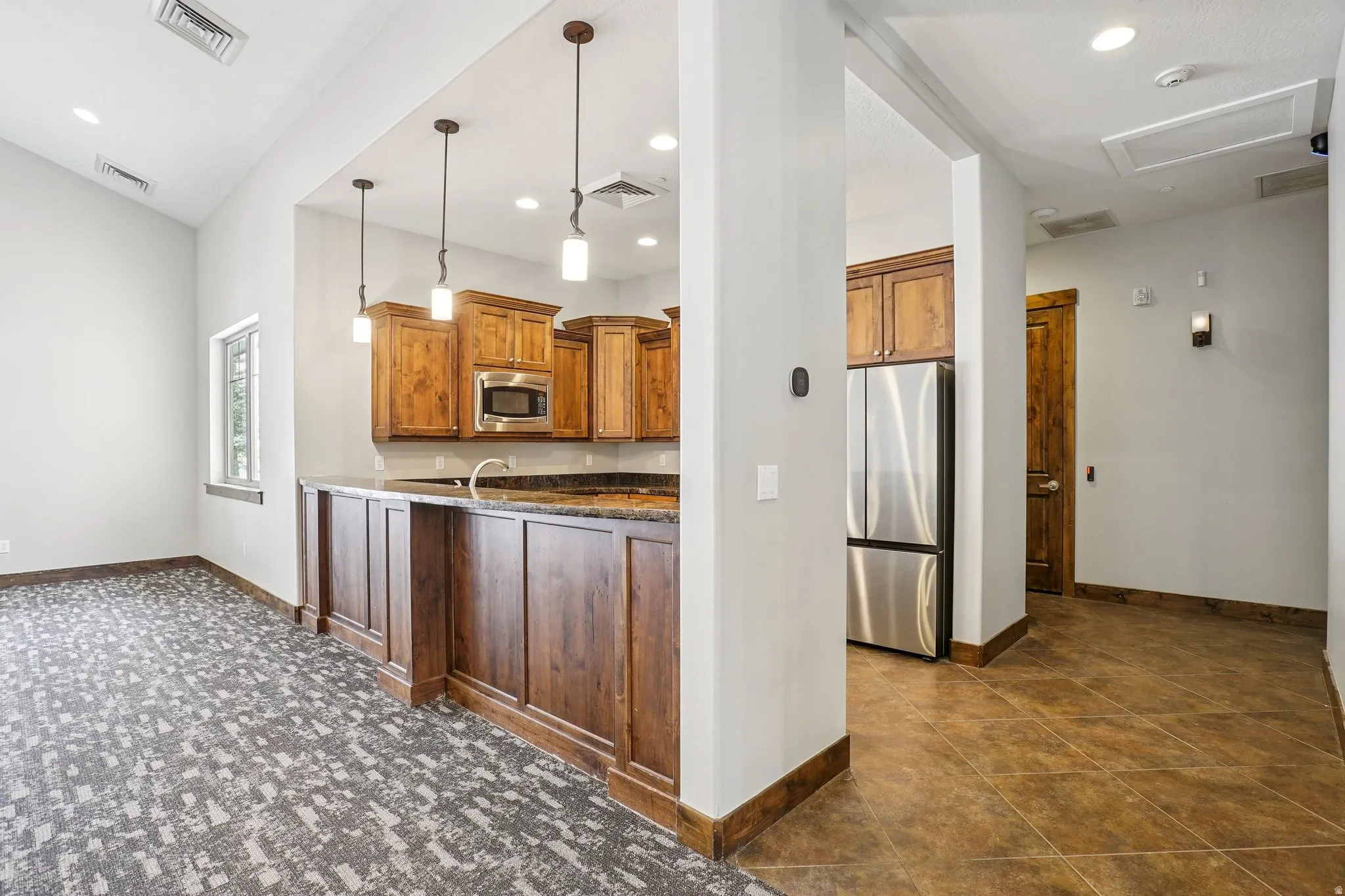 Kitchen with pendant lighting, stainless steel appliances, dark stone countertops, and wood finish cabinetry