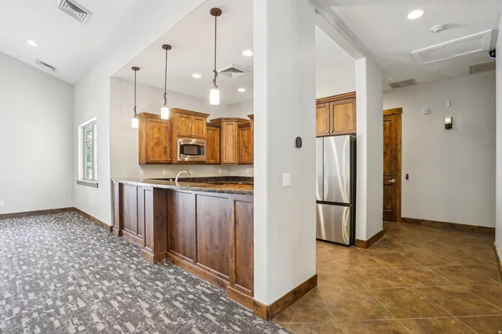 Kitchen with pendant lighting, stainless steel appliances, dark stone countertops, and wood finish cabinetry