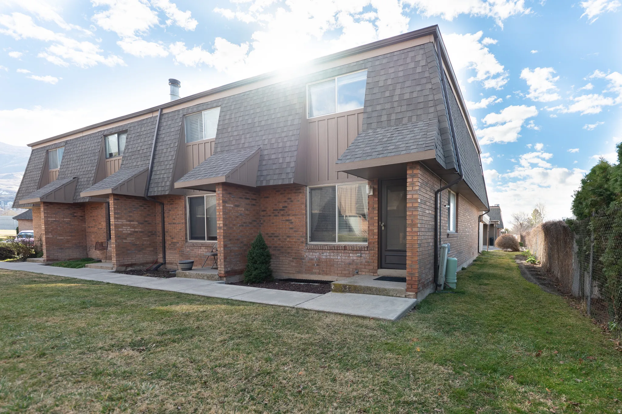 Rear view of property with brick siding, mansard roof, board and batten siding, and a shingled roof