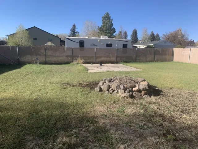 Expansive backyard featuring a rock fire pit, concrete patio area, and chain-link fencing