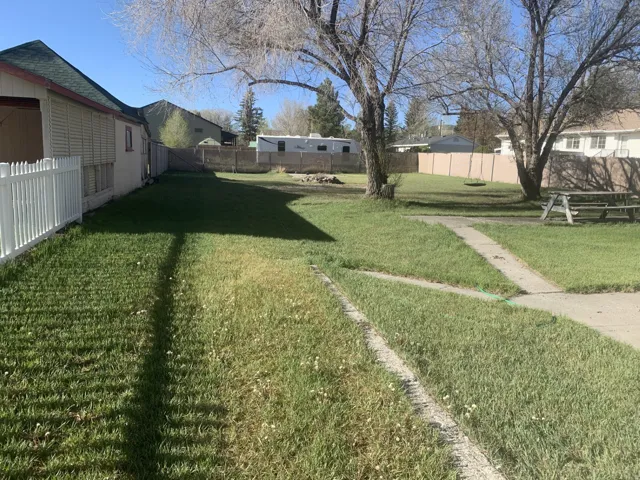 Expansive grassy yard area featuring a concrete pathway, mature trees, and perimeter fencing