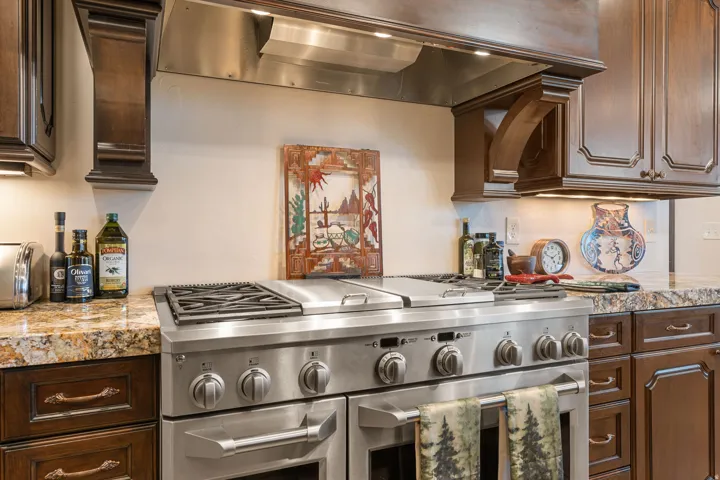 Kitchen with exhaust hood, double oven range, dark wood finish cabinetry, and light stone counters