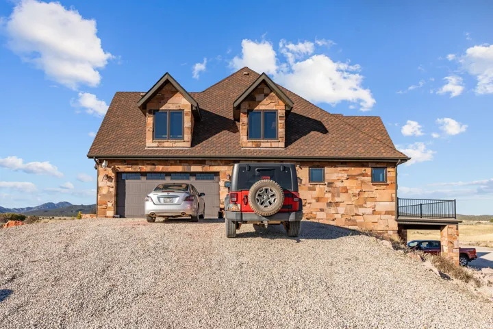 View of front of property with stone siding, a shingled roof, gravel driveway, and a mountain view