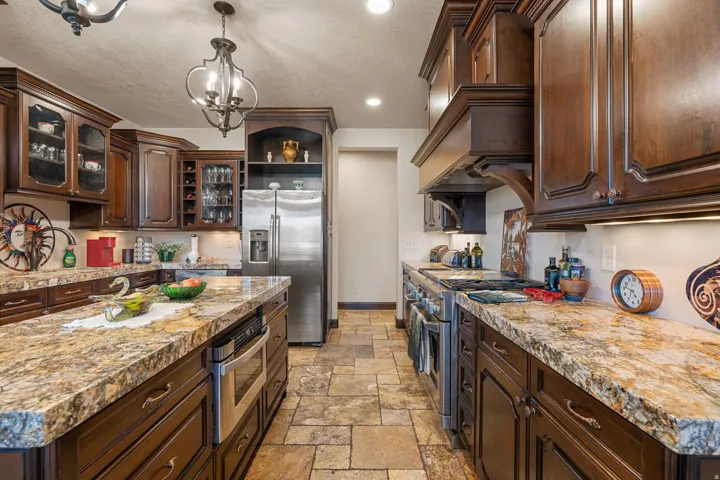 Kitchen with dark wood finish cabinets, stainless steel appliances, stone tile flooring, and a textured ceiling