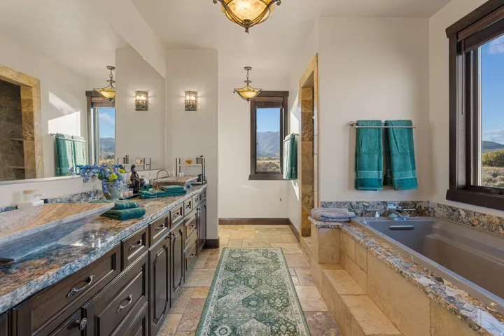 Full bathroom featuring stone tile floors, double vanity, a garden tub, a shower, and a mountain view