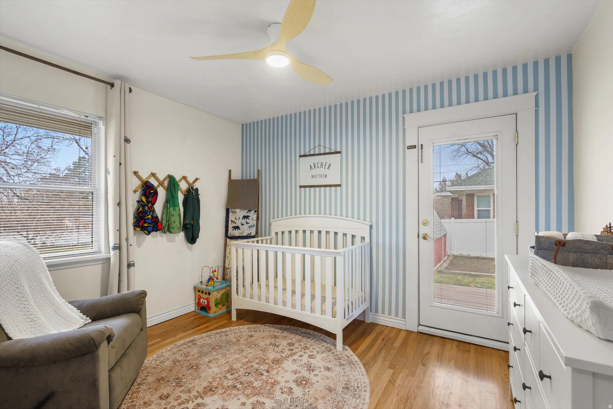 Bedroom featuring light wood-style floors, a ceiling fan, a nursery area, and wallpapered walls