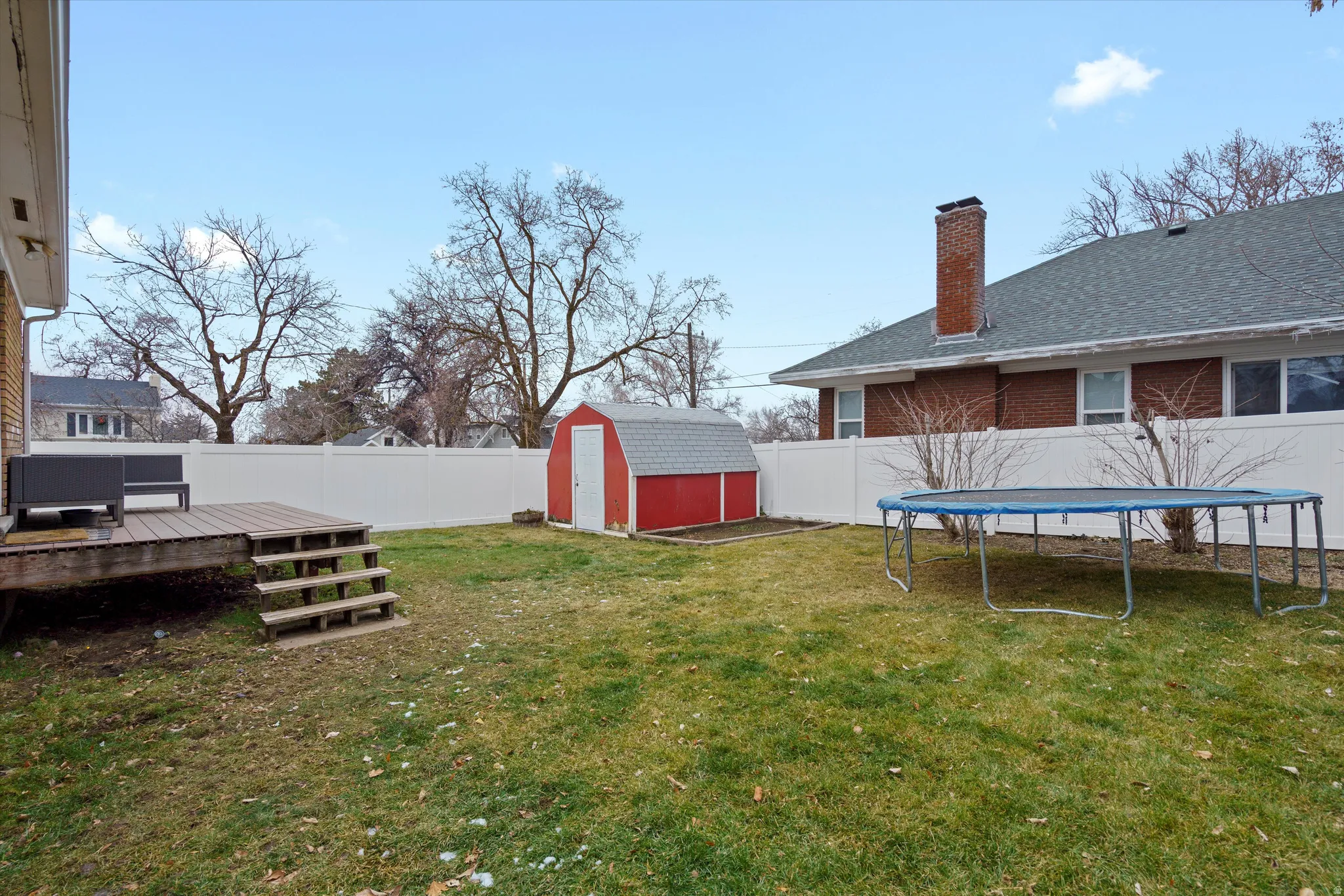 Fenced backyard featuring a storage unit, a deck, and a trampoline