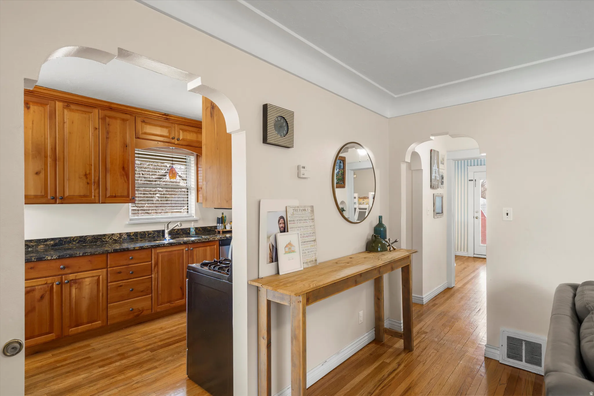 Kitchen featuring dark stone countertops, light wood finished floors, wood finish cabinetry, arched walkways, and black gas stove