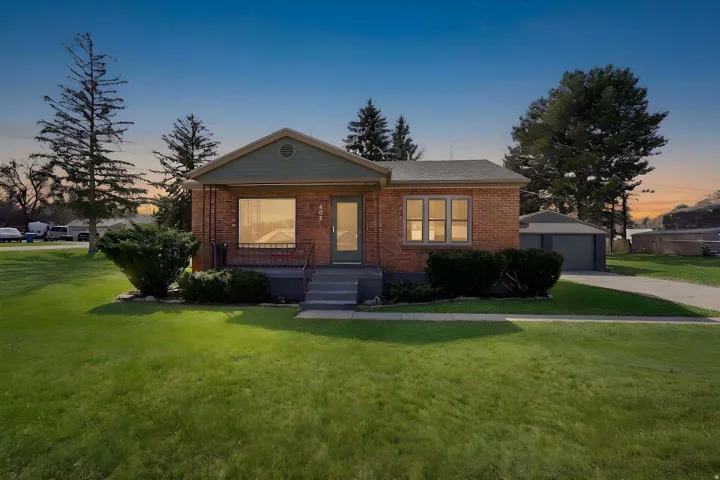 View of front of property with brick siding, a yard, a detached garage, and an outdoor structure