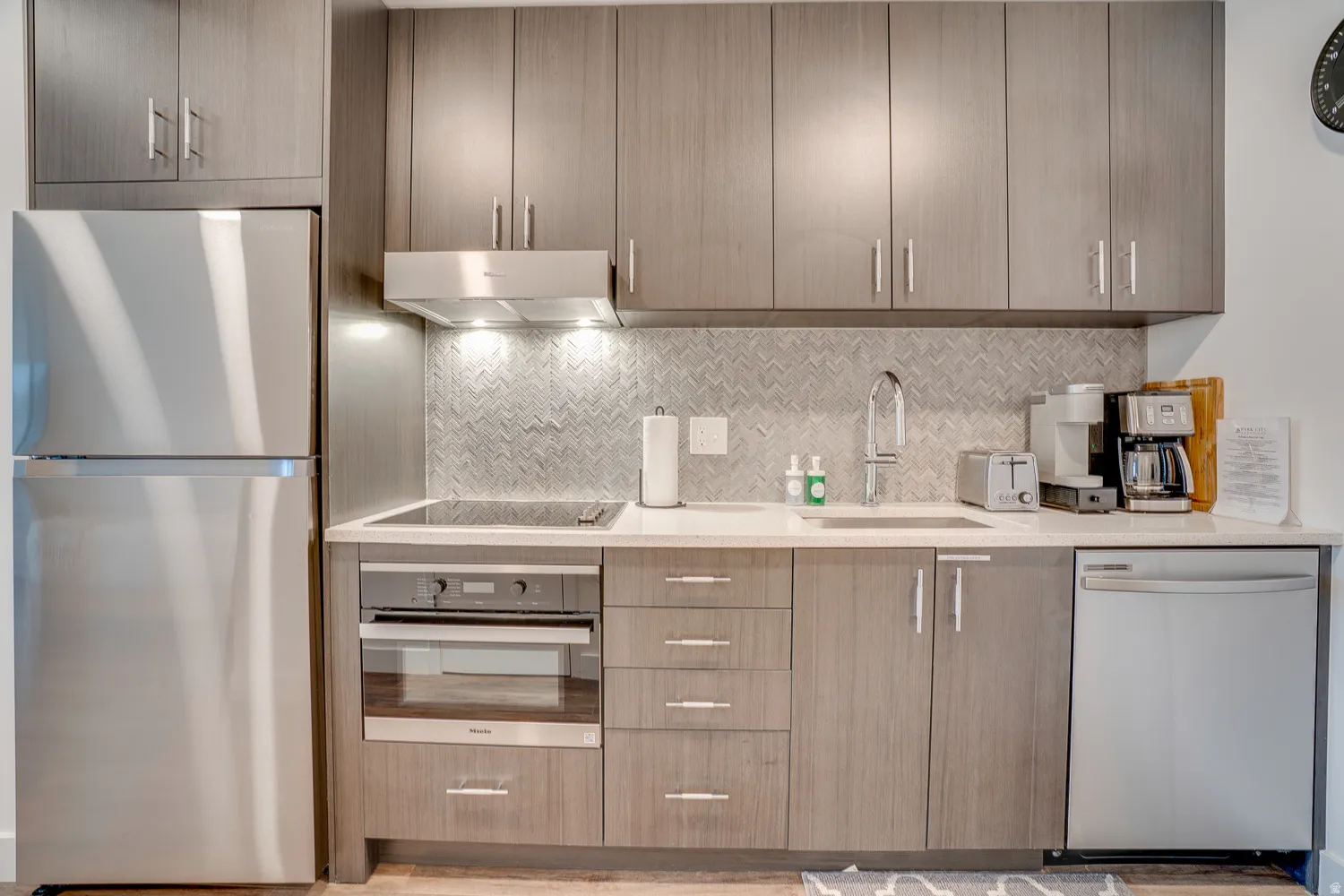 Kitchen featuring stainless steel appliances, modern cabinets, light stone countertops, and backsplash