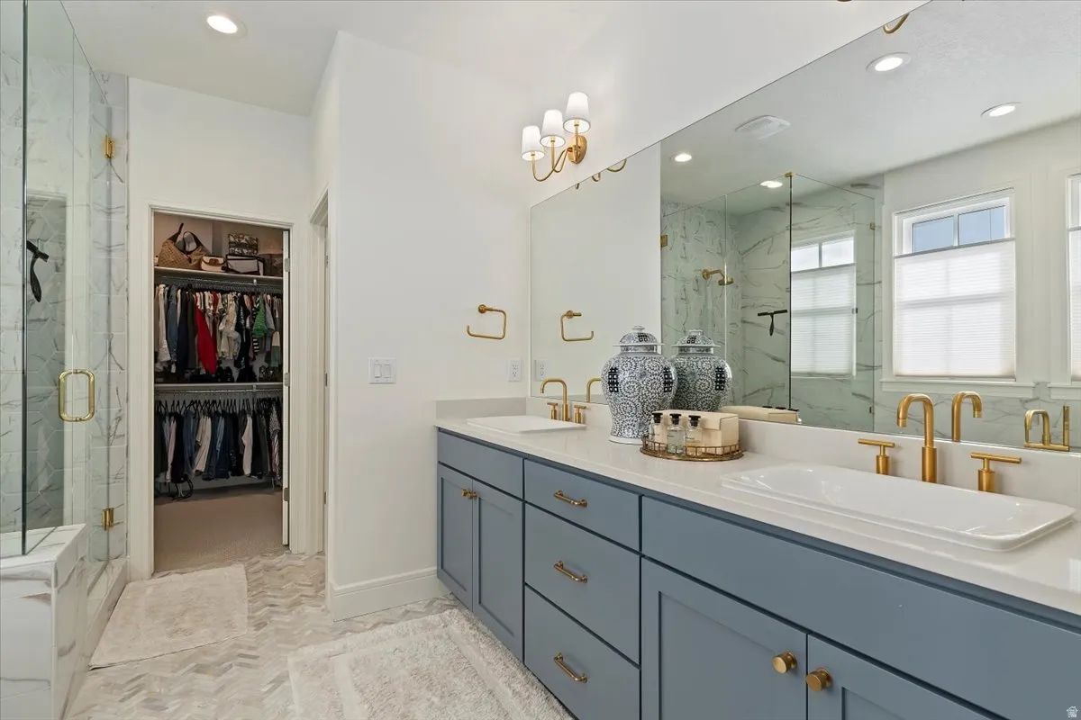 Bathroom featuring double vanity, a marble finish shower, a spacious closet, and recessed lighting