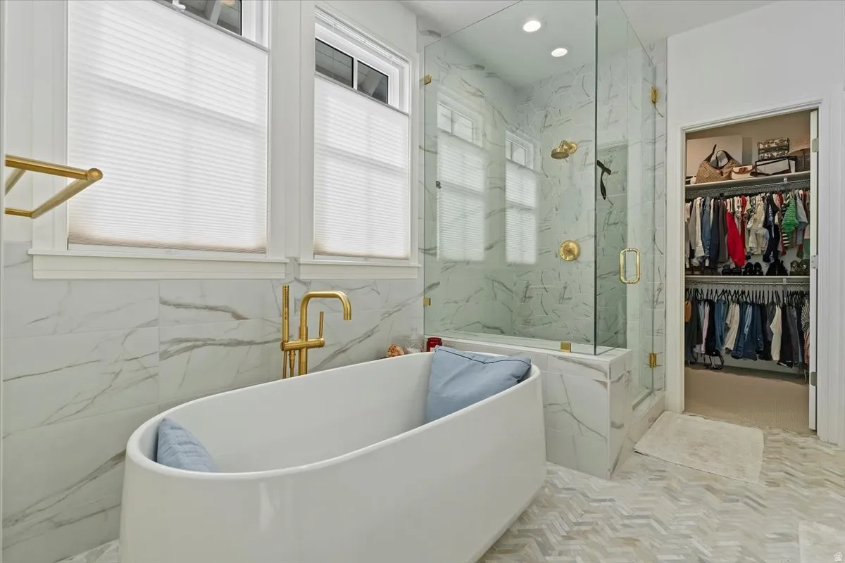 Bathroom featuring a walk in closet, a soaking tub, a marble finish shower, recessed lighting, and tile walls