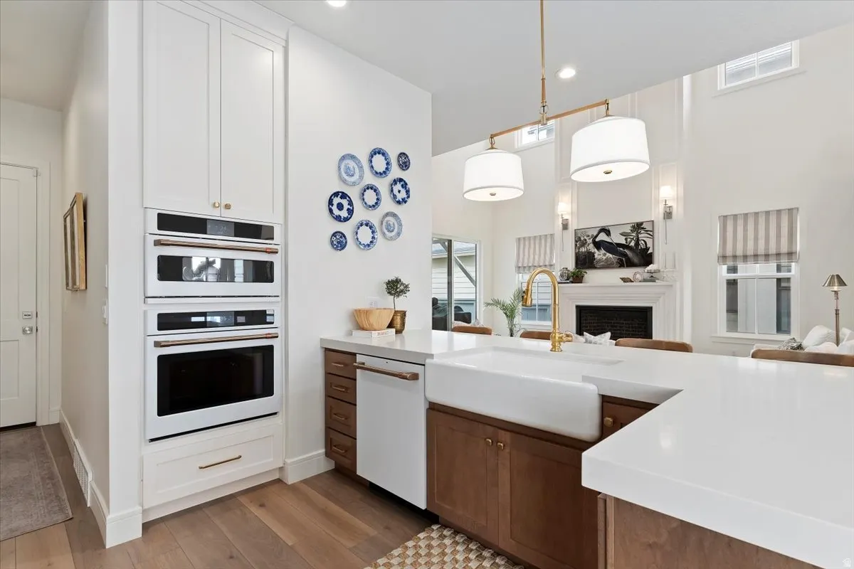 Kitchen with dual tone cabinets, open floor plan, white appliances, hanging light fixtures, and light stone counters