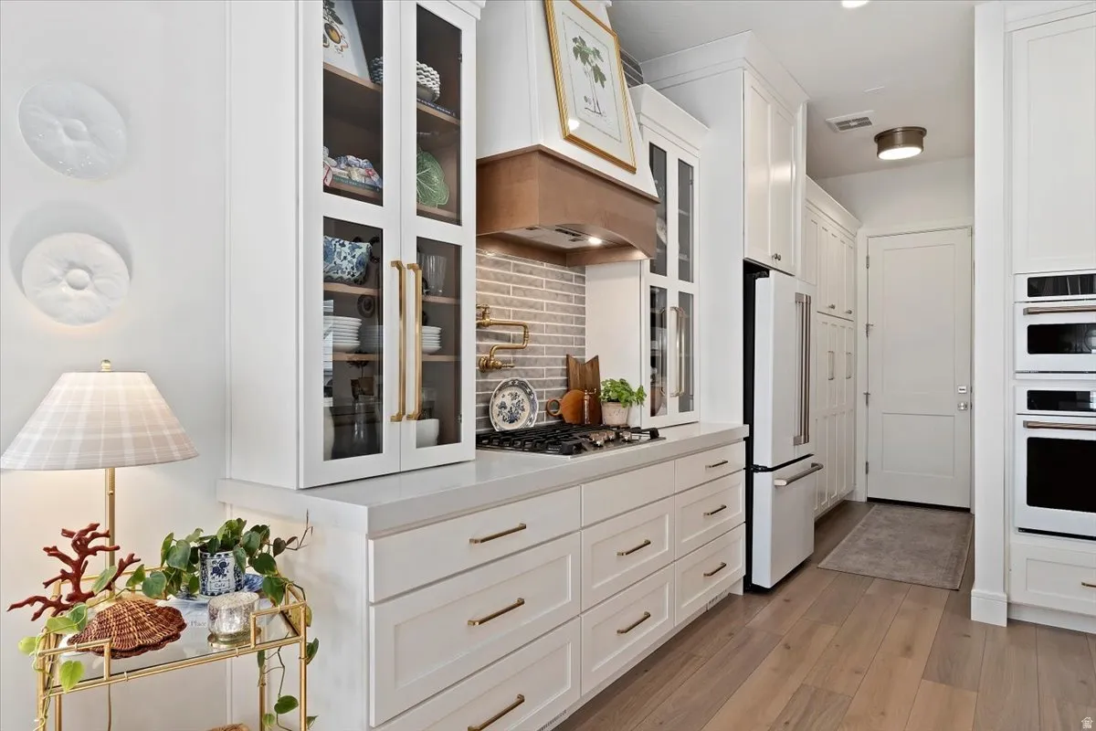 Kitchen with white cabinetry, light wood-style floors, white appliances, and glass fronted cabinets