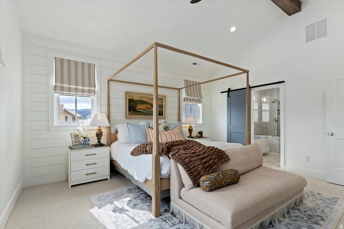 Bedroom with a barn door, light colored carpet, ensuite bath, vaulted ceiling, and a ceiling fan