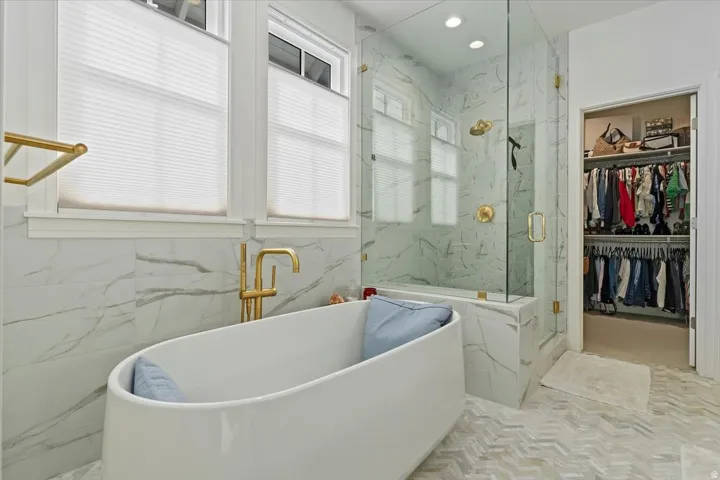 Bathroom featuring a walk in closet, a soaking tub, a marble finish shower, recessed lighting, and tile walls