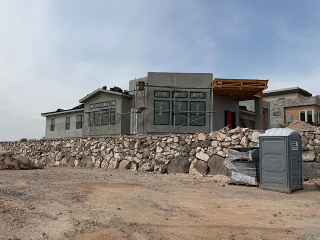 Architectural stucco exterior with multiple window configurations, a wood-frame patio cover, and a substantial stone retaining wall