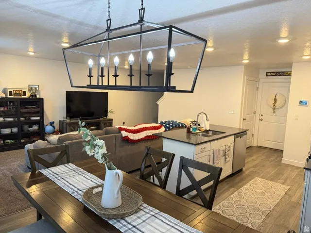 Open concept living area featuring a prominent chandelier, recessed lighting, a kitchen island with a sink, and wood-finish flooring