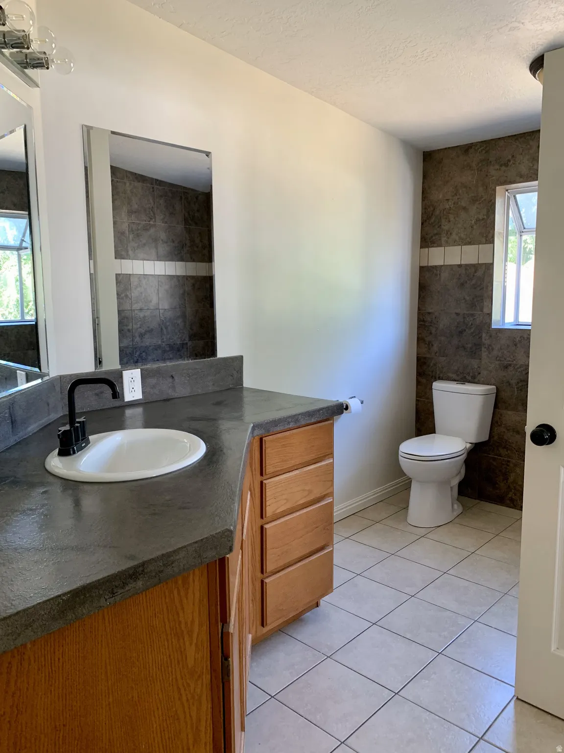 Bathroom featuring plenty of natural light, vanity, light tile patterned floors, a textured ceiling, and tile walls