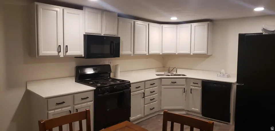 Kitchen with black appliances, white cabinets, light countertops, and recessed lighting