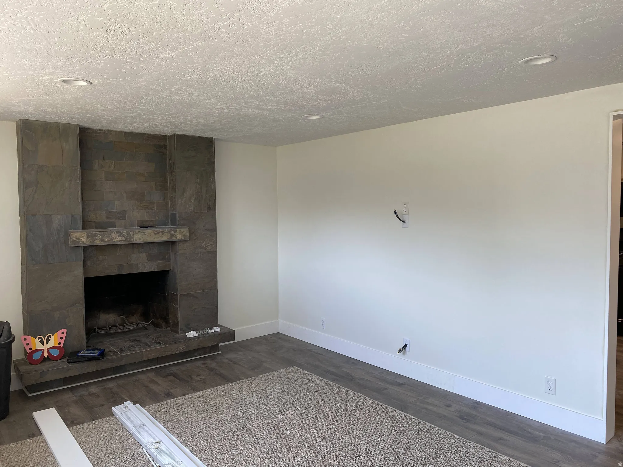 Unfurnished living room with dark wood-type flooring, a large fireplace, and a textured ceiling