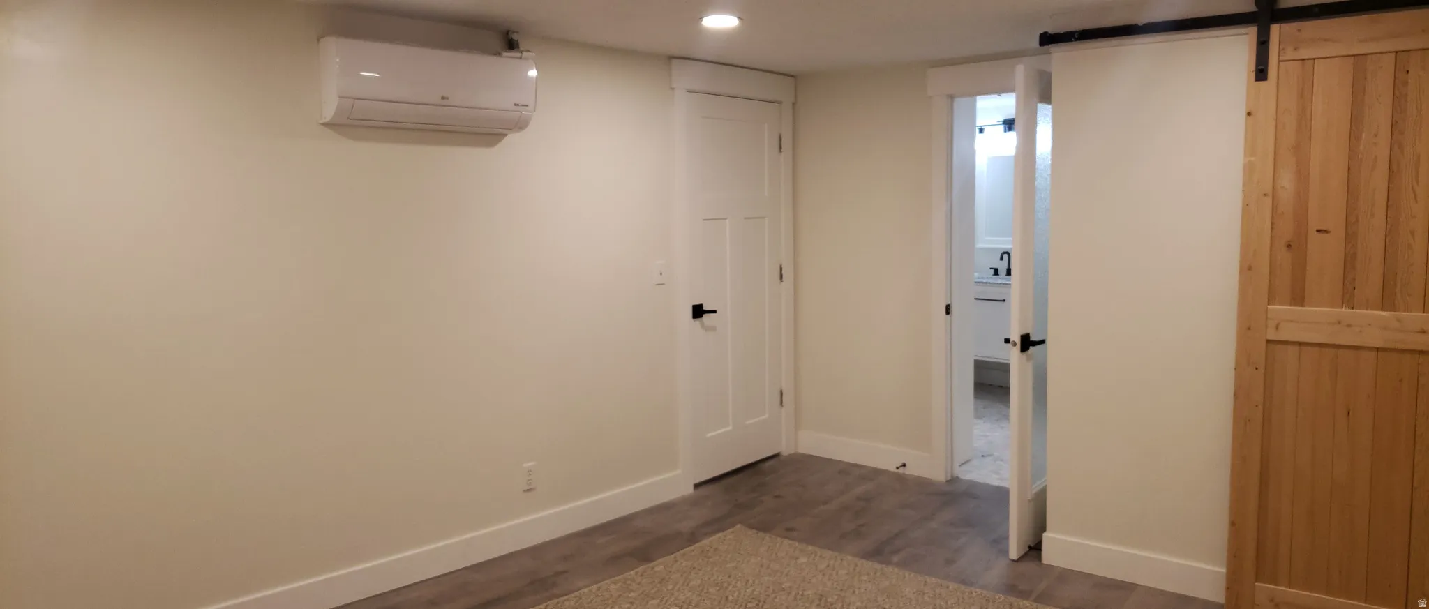 Finished basement with dark wood-type flooring, a barn door, and recessed lighting