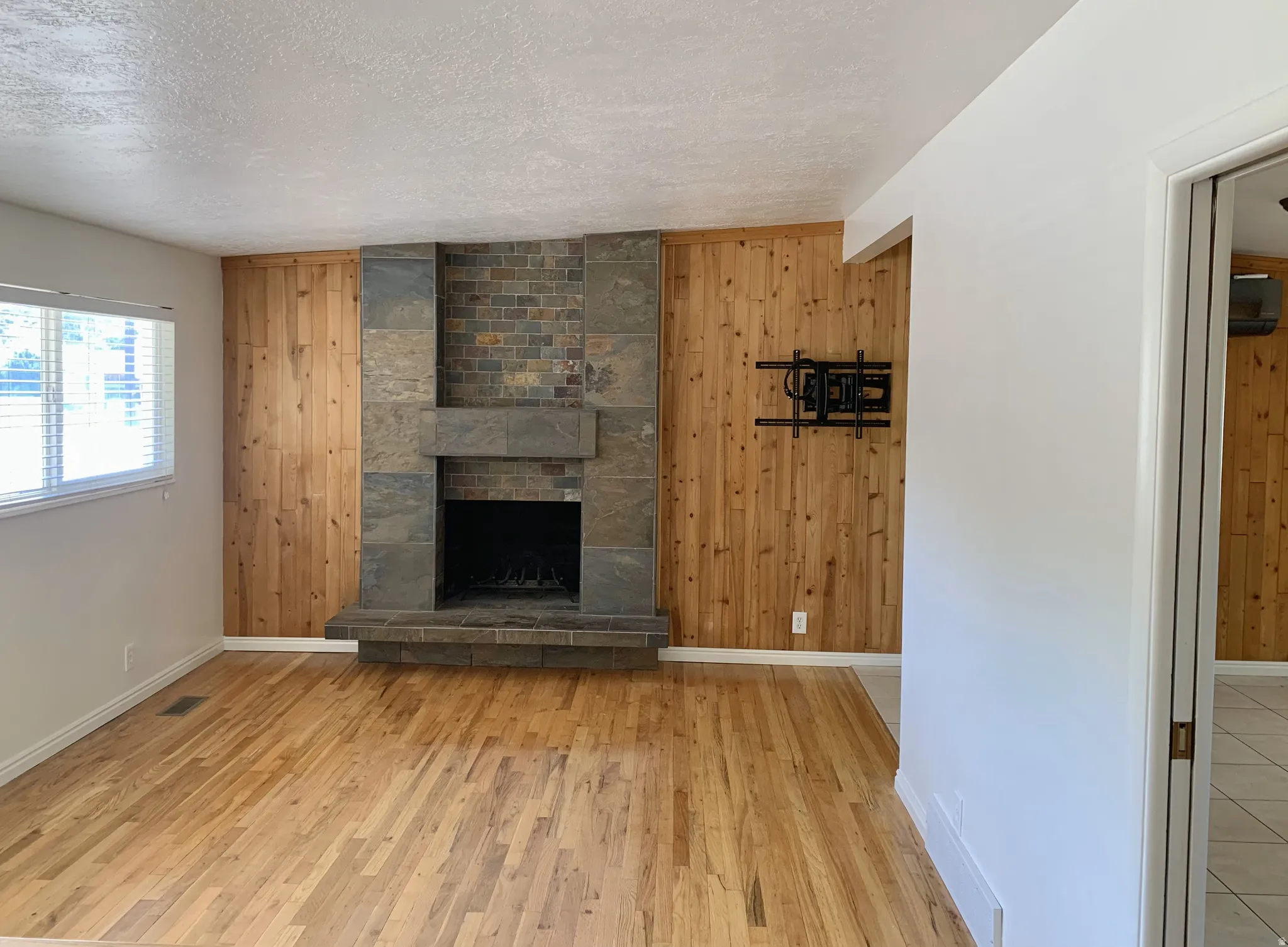Unfurnished living room with wooden walls, wood finished floors, a textured ceiling, and a fireplace