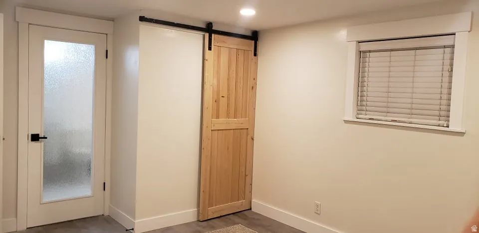 Unfurnished bedroom with a barn door, dark wood-type flooring, multiple windows, and recessed lighting