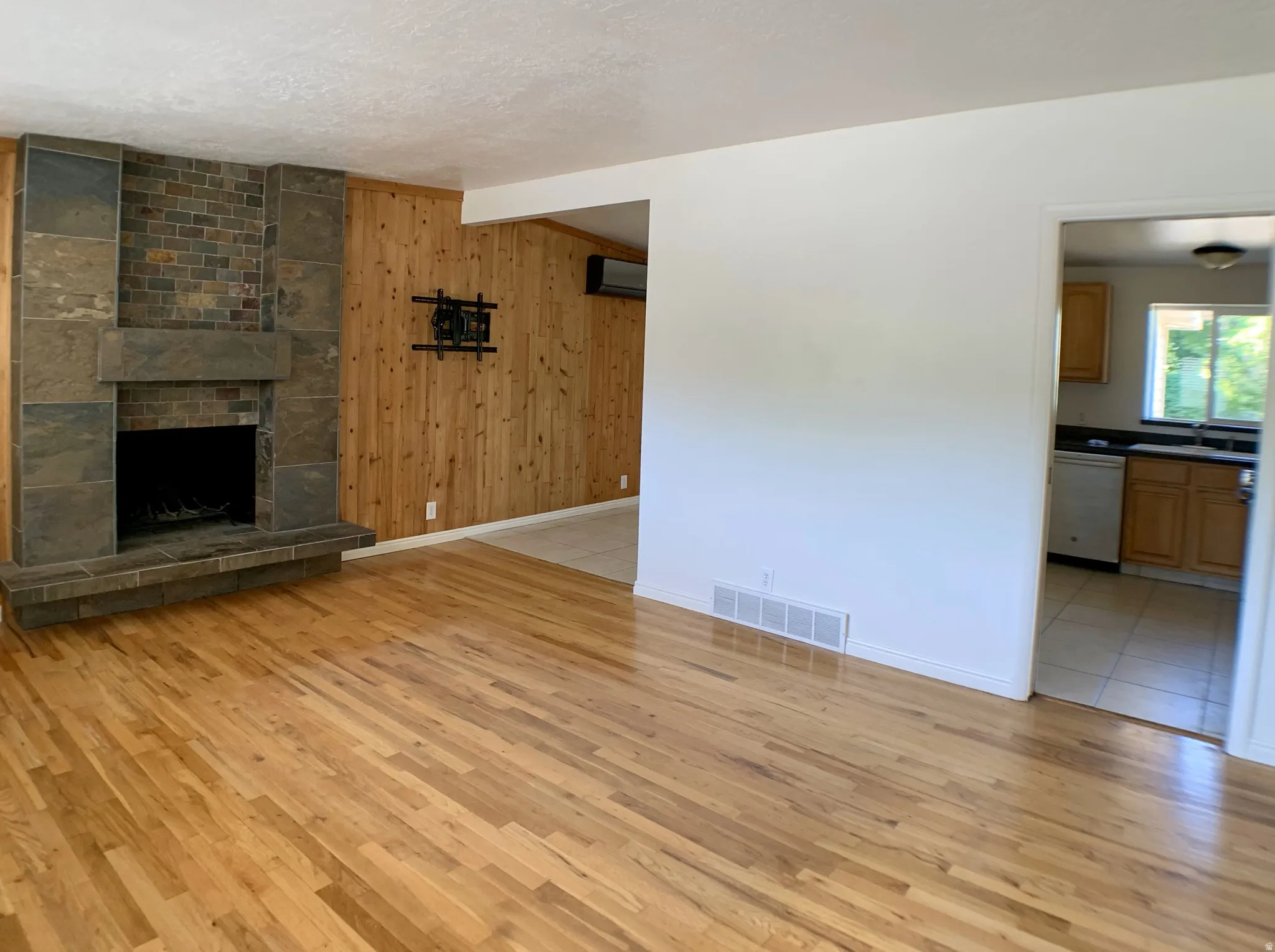 Unfurnished living room with wood walls, light wood-type flooring, a stone fireplace, a textured ceiling, and beamed ceiling