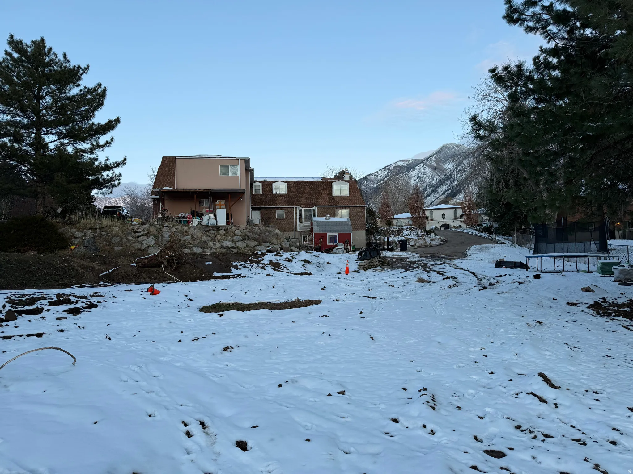 Snow covered house featuring a trampoline, a mountain view, a gambrel roof, and a balcony