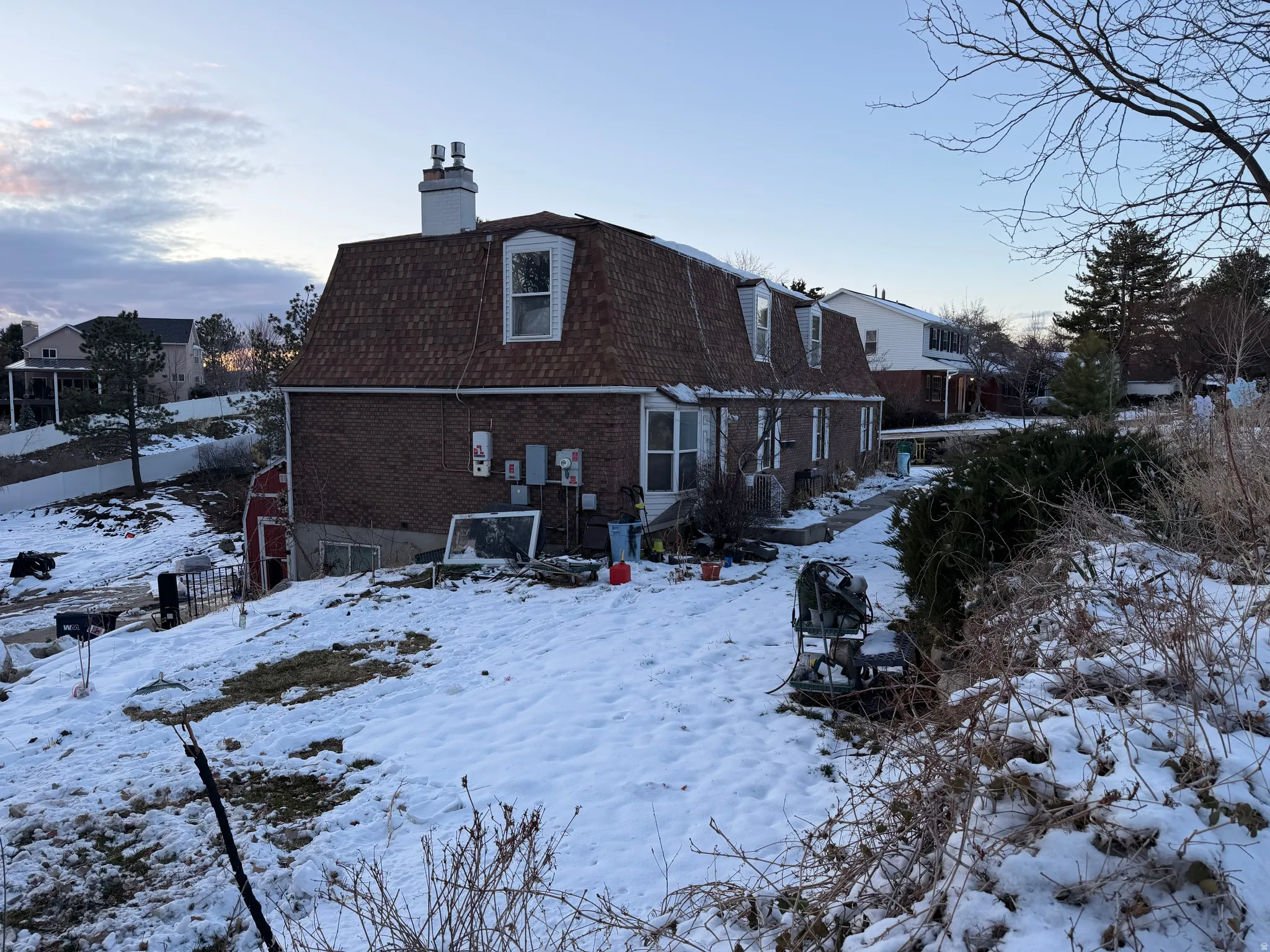 Rear view of property featuring brick siding, a chimney, mansard roof, and roof with shingles