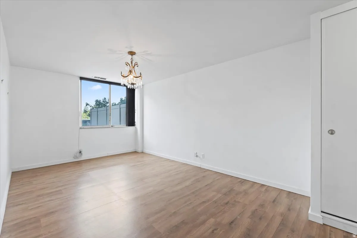 Bright room featuring wood-finish flooring, a large window, a decorative chandelier, white walls, and a white bi-fold closet door