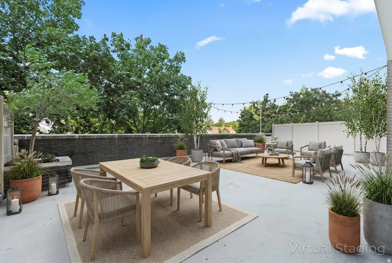 Expansive outdoor patio featuring a concrete surface, a low stone privacy wall, string lighting, and mature perimeter trees