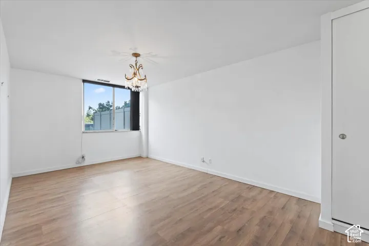 Bright room featuring wood-finish flooring, a large window, a decorative chandelier, white walls, and a white bi-fold closet door