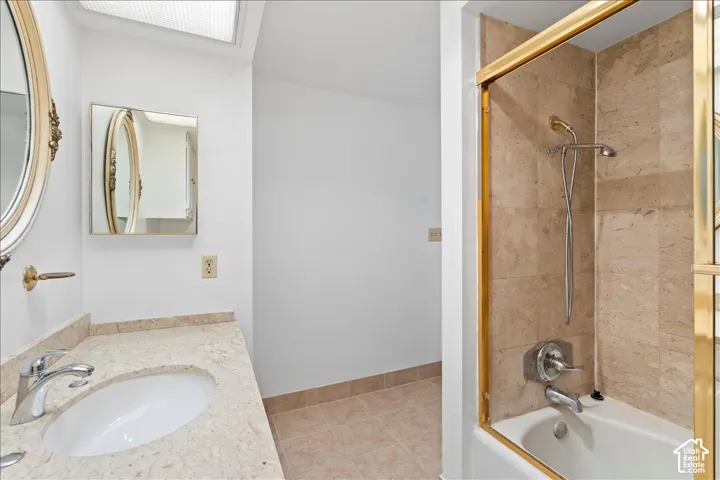 Full bathroom with bath / shower combo with glass door, vanity, and light tile patterned floors