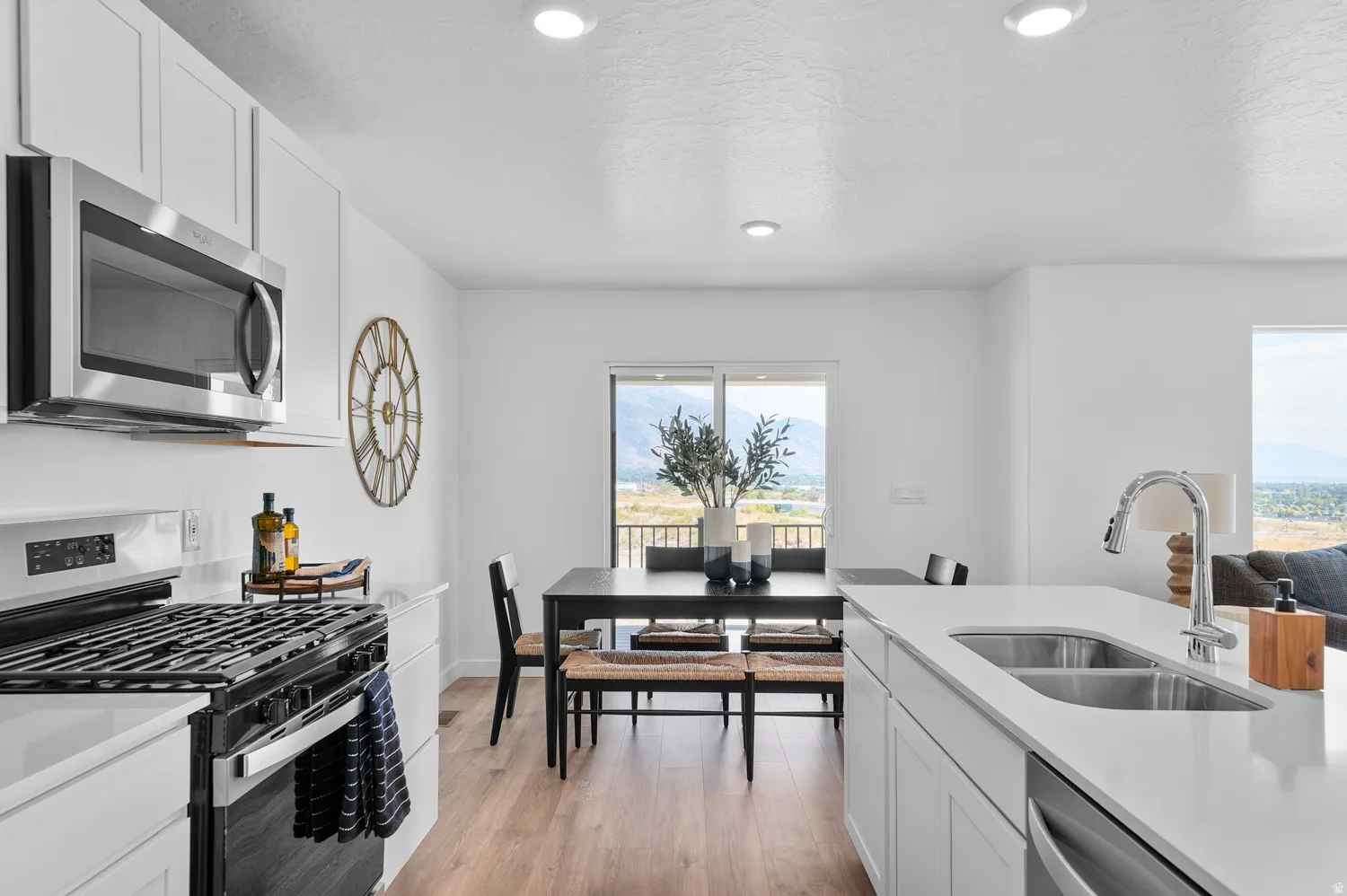 Kitchen with stainless steel appliances, white cabinets, light wood-type flooring, light stone counters, and recessed lighting