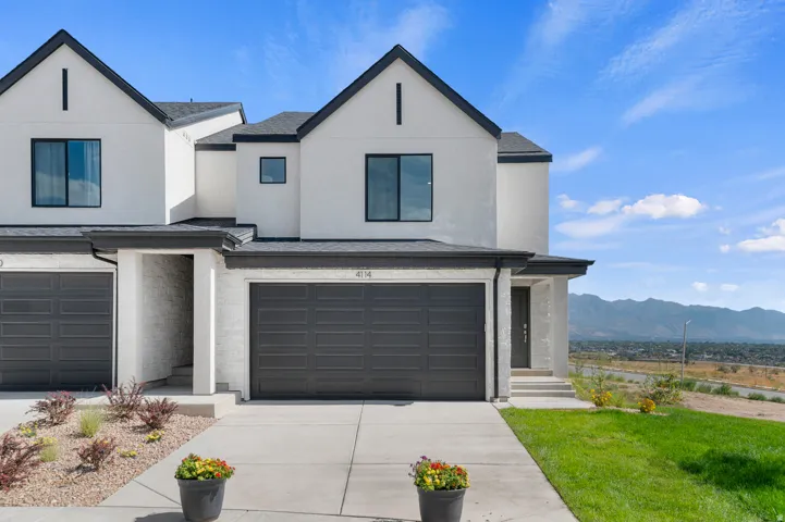 View of front of house with stucco siding, a mountain view, a garage, concrete driveway, and a front lawn